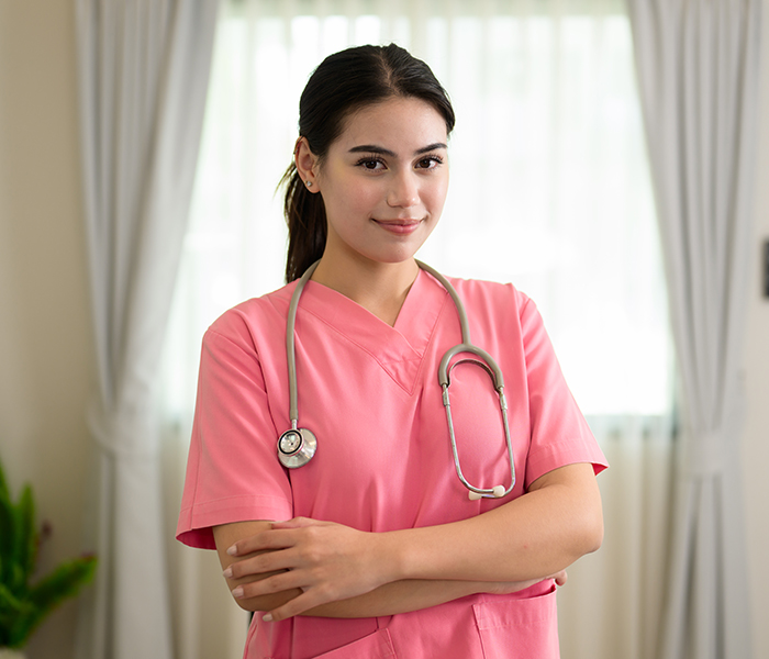 A headshot of a smiling caregiver in pink scrubs wearing a stethoscope.